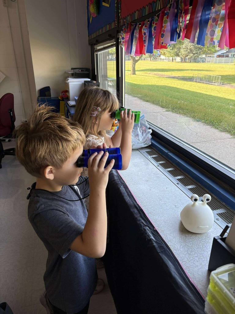 Two young learners standing, looking out a window with binoculars.