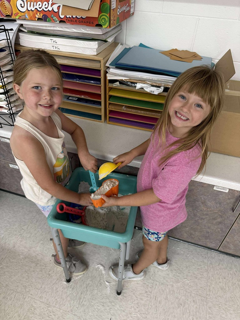 Two young learners standing at a sandbox and playing.