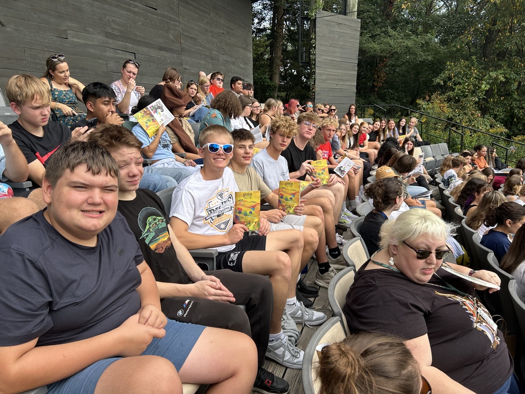 Students sitting in seats at an outdoor play.