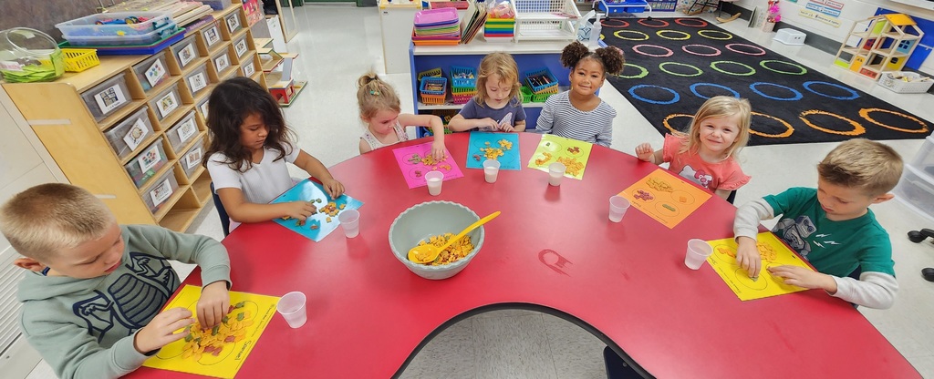 Young learners sitting at a table, giving the thumbs up with goldfish crackers sorted in front of them.