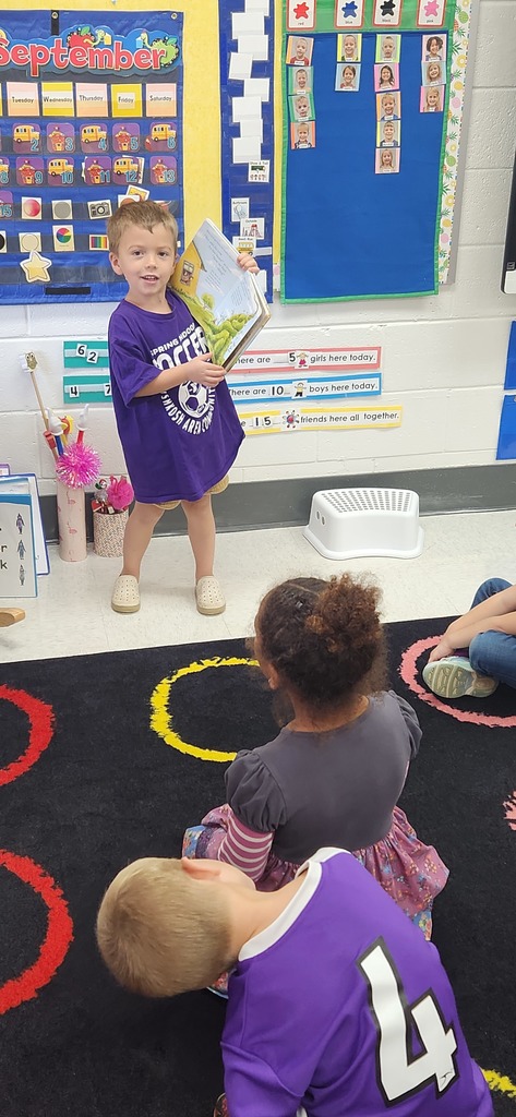 An early elementary learner stands in front of a class sharing a book.