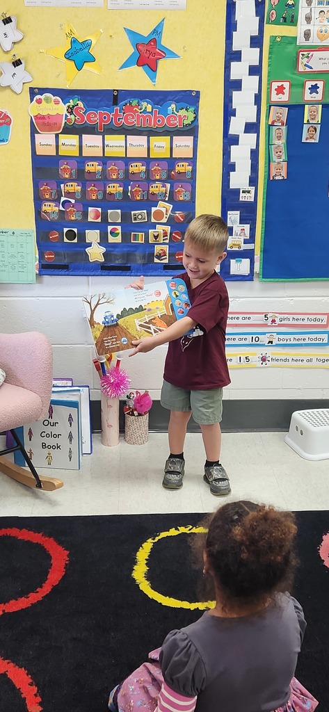 An early elementary learner stands in front of a class sharing a book.