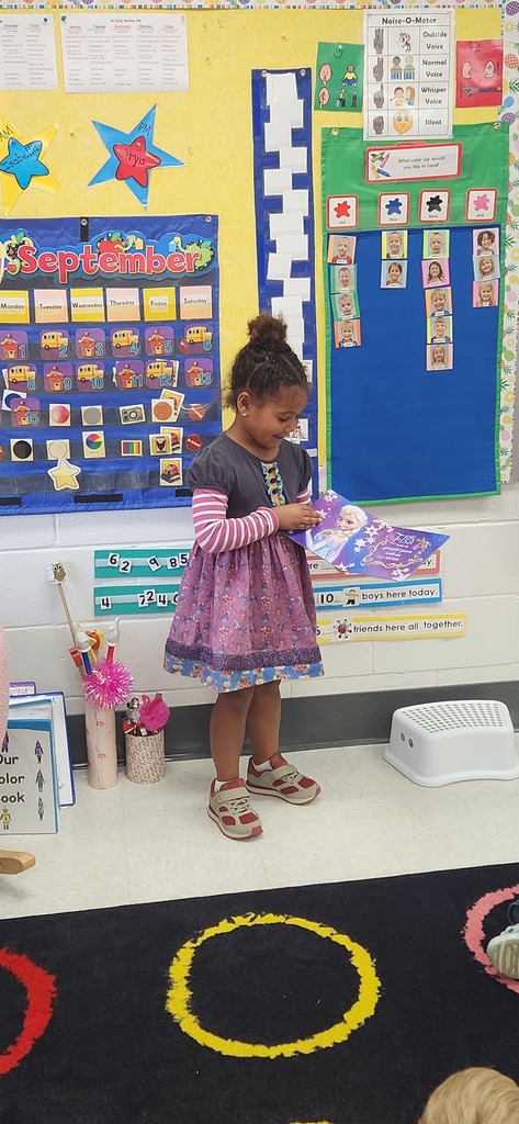 An early elementary learner stands in front of a class sharing a book.
