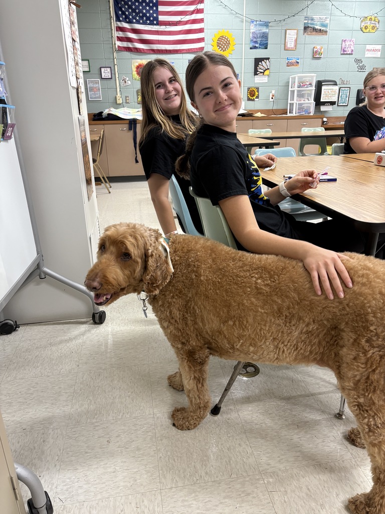 High school students sitting at a table while petting a dog named Griffin.
