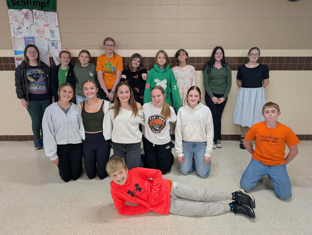 Middle school st udents dressed in orange, green, and white huddle togehter for a group photo.