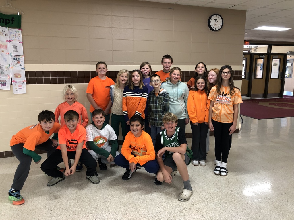 Middle school st udents dressed in orange, green, and white huddle togehter for a group photo.