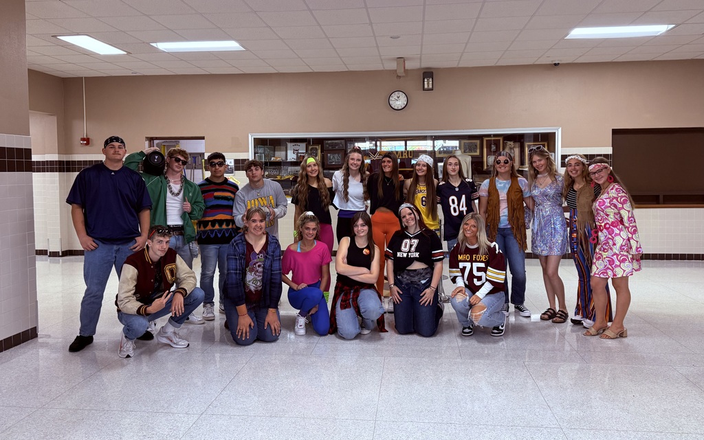 High school students, wearing clothes from various decades, stand together for a photo. 