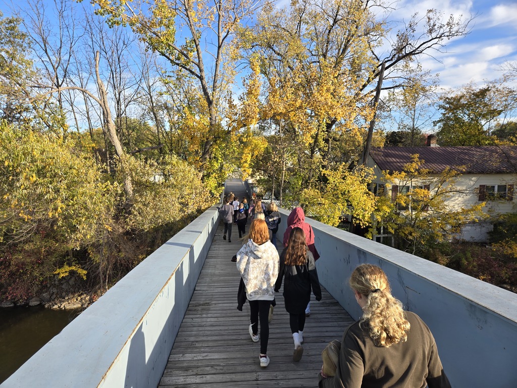 Middle school students on a walking bridge with trees in the background.
