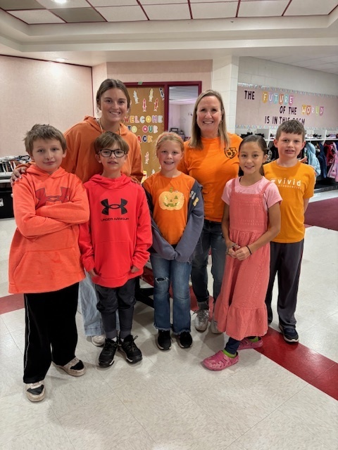 A group of 5 elementary students and two adults, wearing orange, standing together for a picture. 