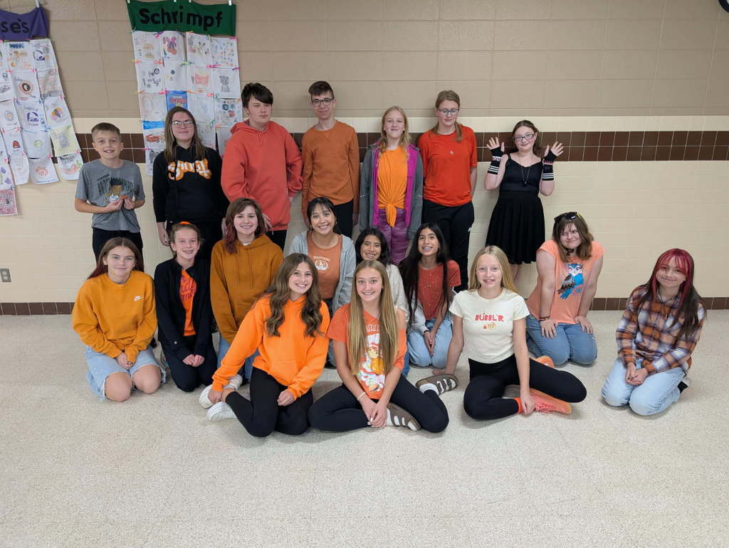 A group of middle school students, wearing orange, gathered together for a picture. 