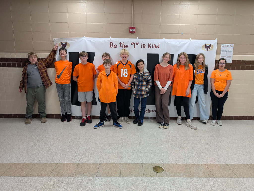 A group of middle school students, wearing orange, gathered together for a picture. 