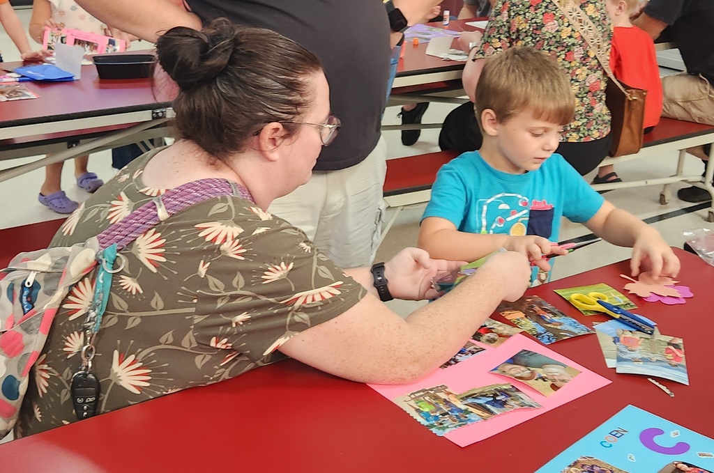 An adult and early elementary student working together with pictures and scissors at a table.