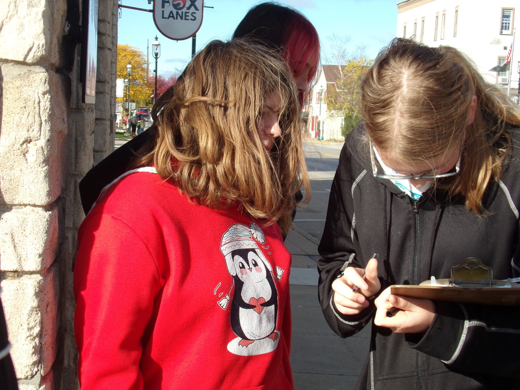 Three middle school students looking at a clipboard of information while outside a building.