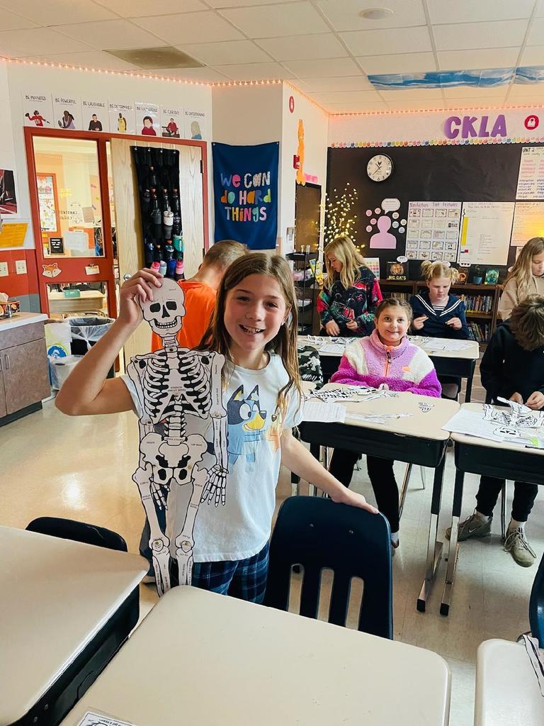 Upper elementary student holding a model of a paper skeleton.