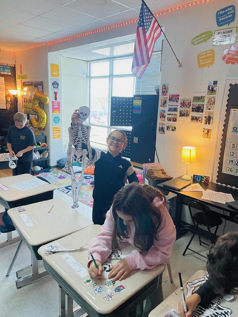 A student holding up a paper model of a skeleton.