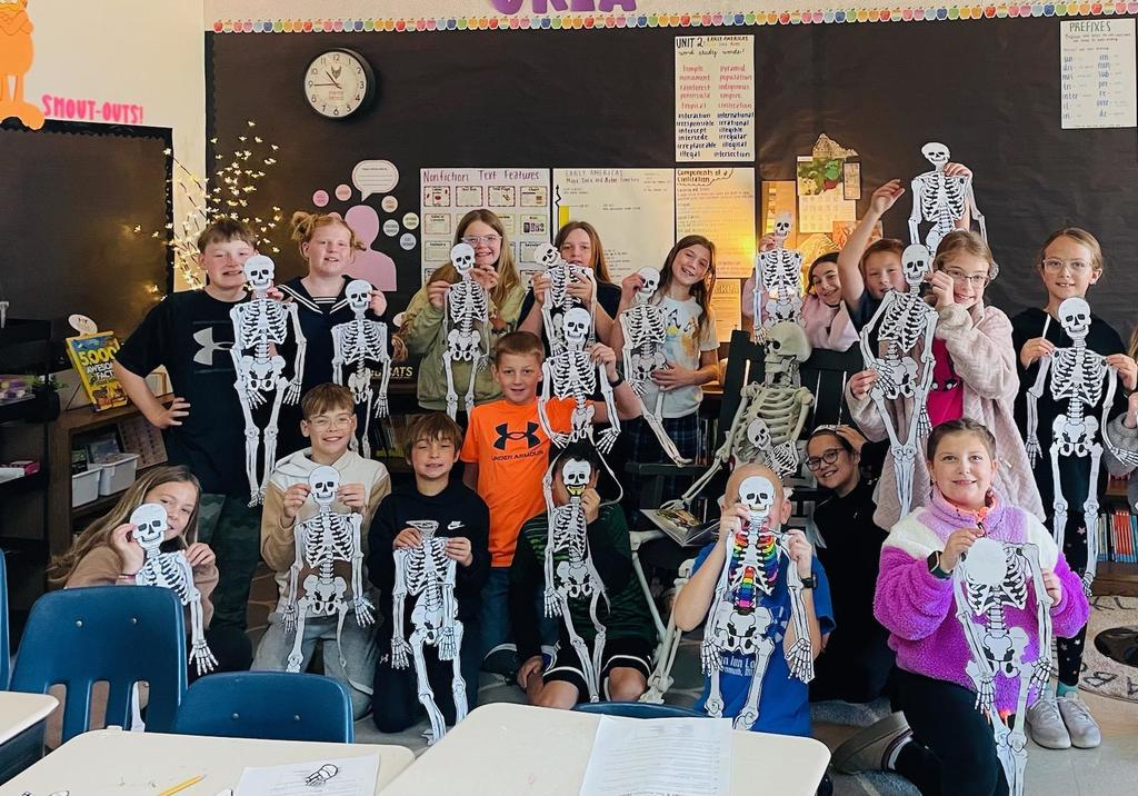 Elementary class holding up paper skeletons.
