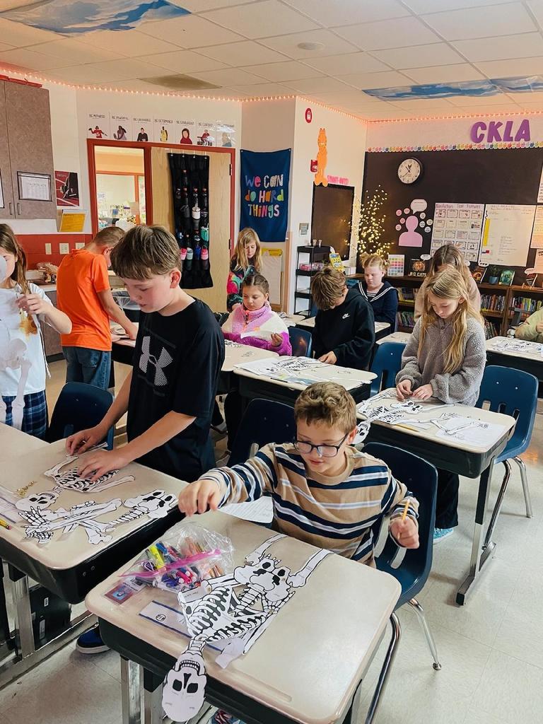 Upper elementary students building paper models of skeletons.