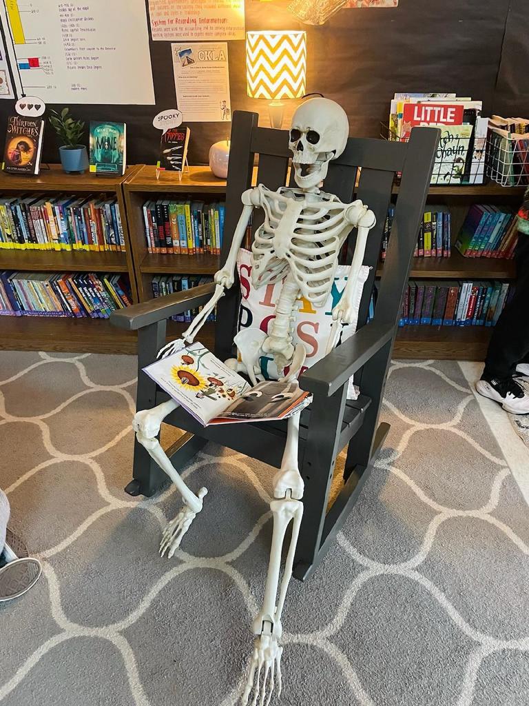 A picture of a skeleton sitting in a chair, reading a book.