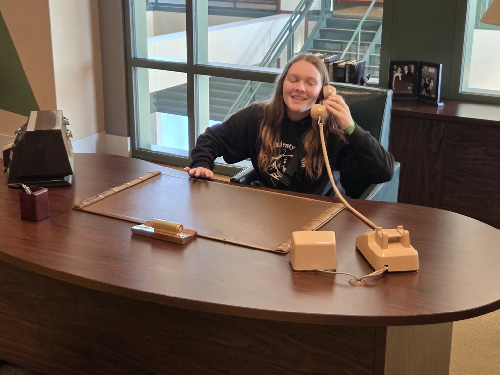 Picture of a high school student sitting at a desk, picking up a phone.