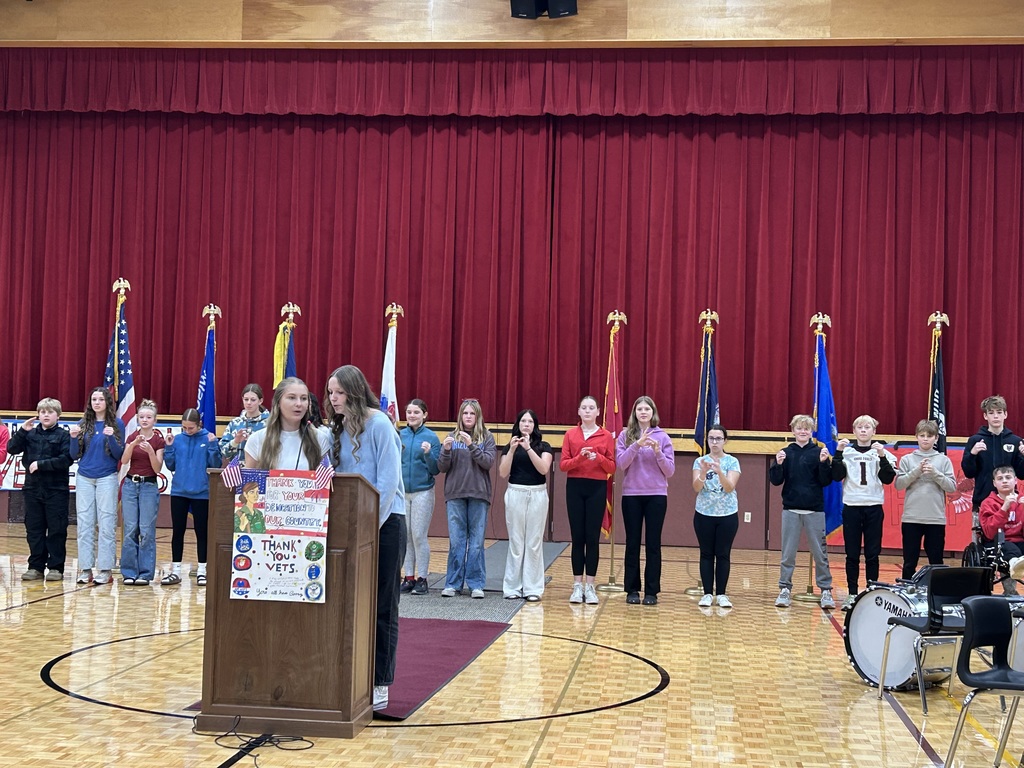 Middle school students doing the Pledge of Allegiance in sign language with two high school students at a podium in front of them.