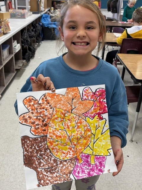 Elementary student holding up her art work in front of her.