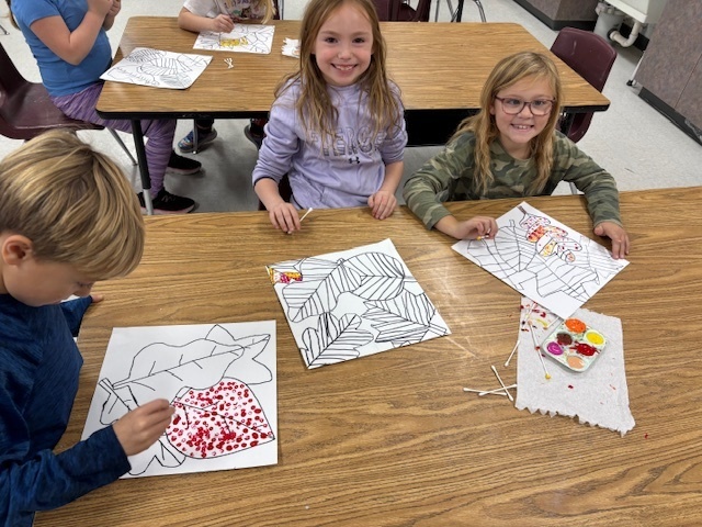 Elementary students working on art work at a table with paint trays in front of them.
