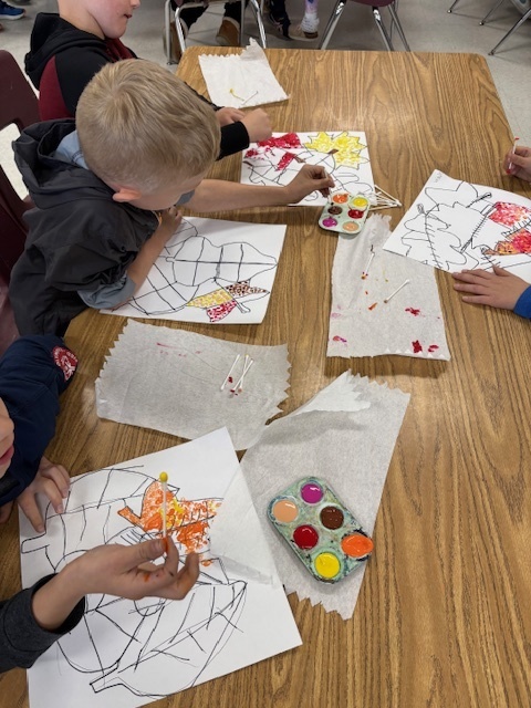 Elementary students working on art work at a table with paint trays in front of them.