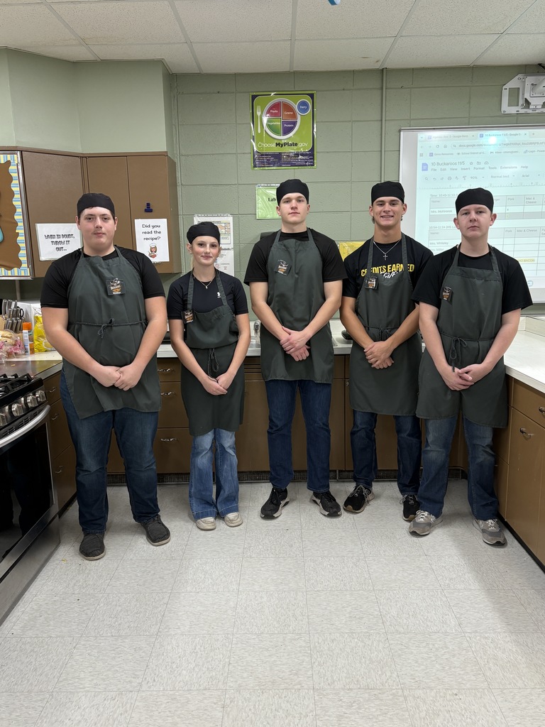 5 high school students standing in a line wearing aprons. 