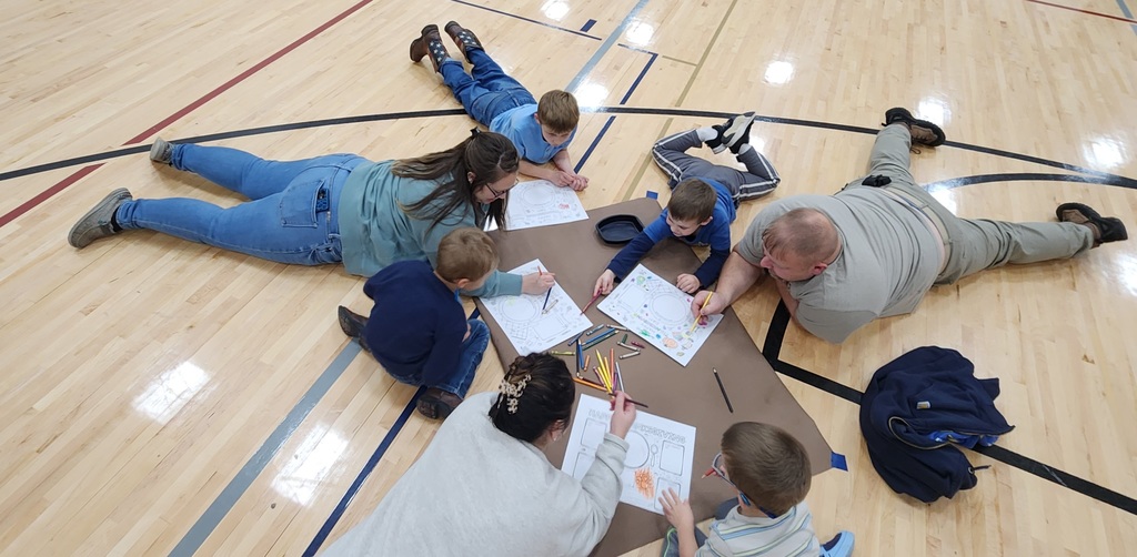 Families laying on a gym floor, working together on projects. 
