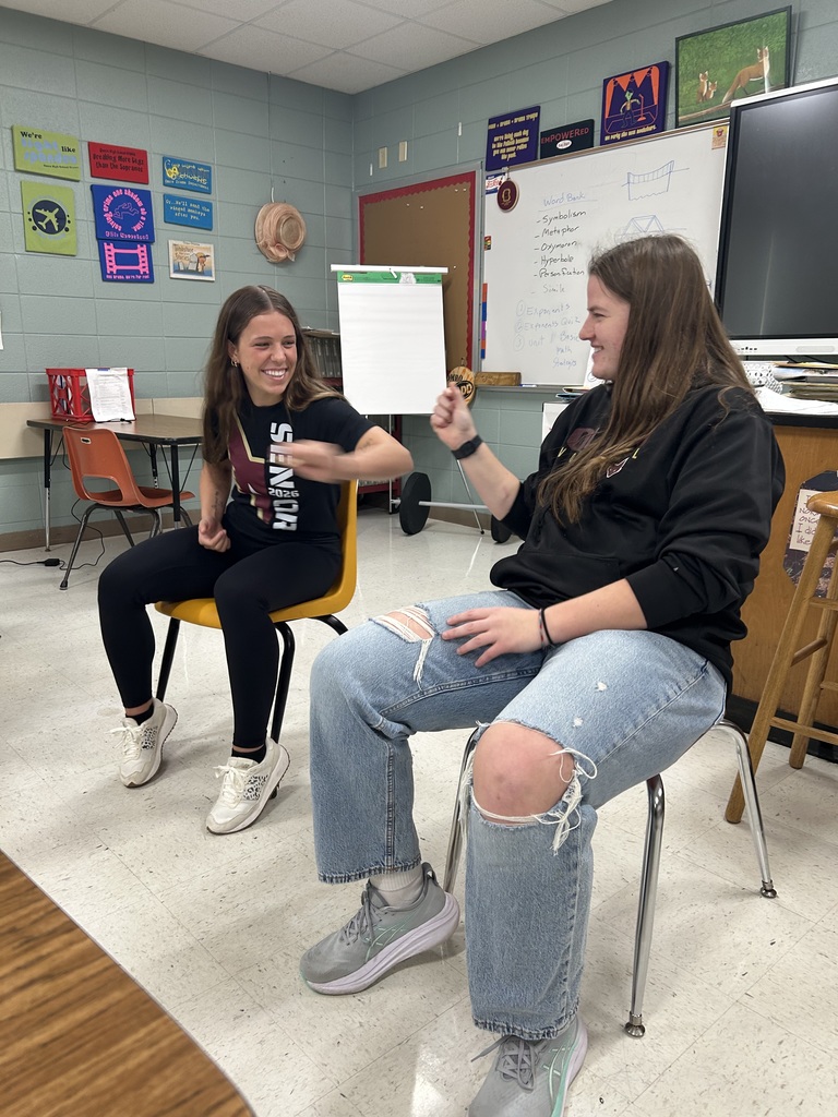 Two high school students playing rock paper scisorrs while sitting in chairs.