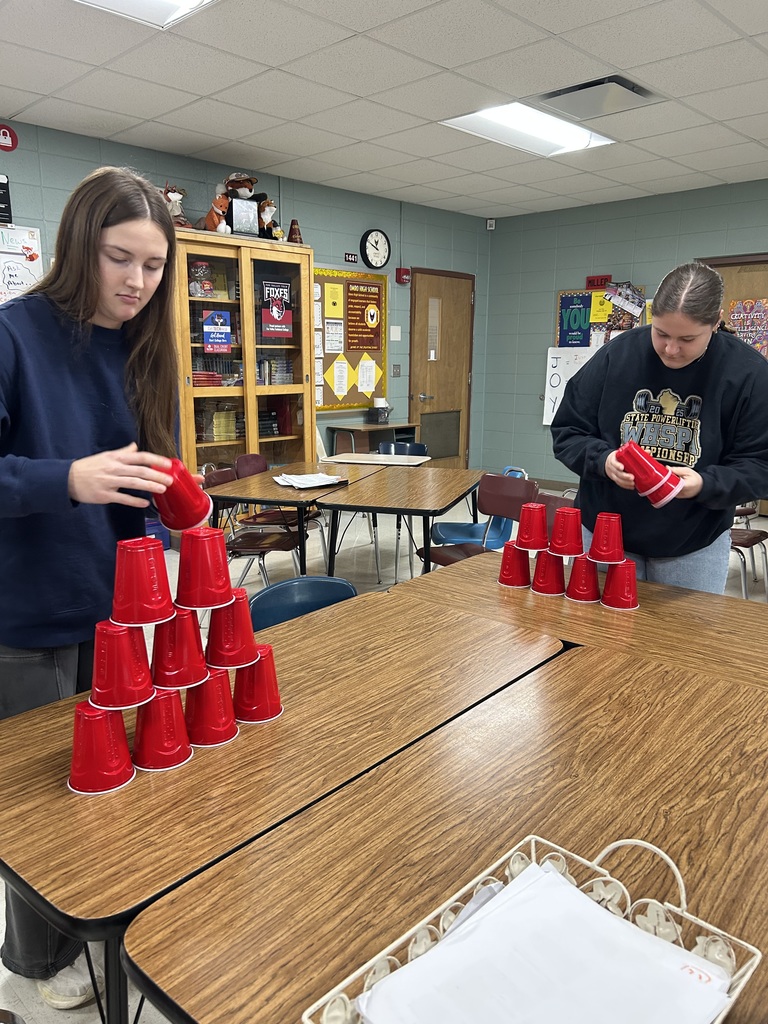 Two high school students cup stacking on tables.