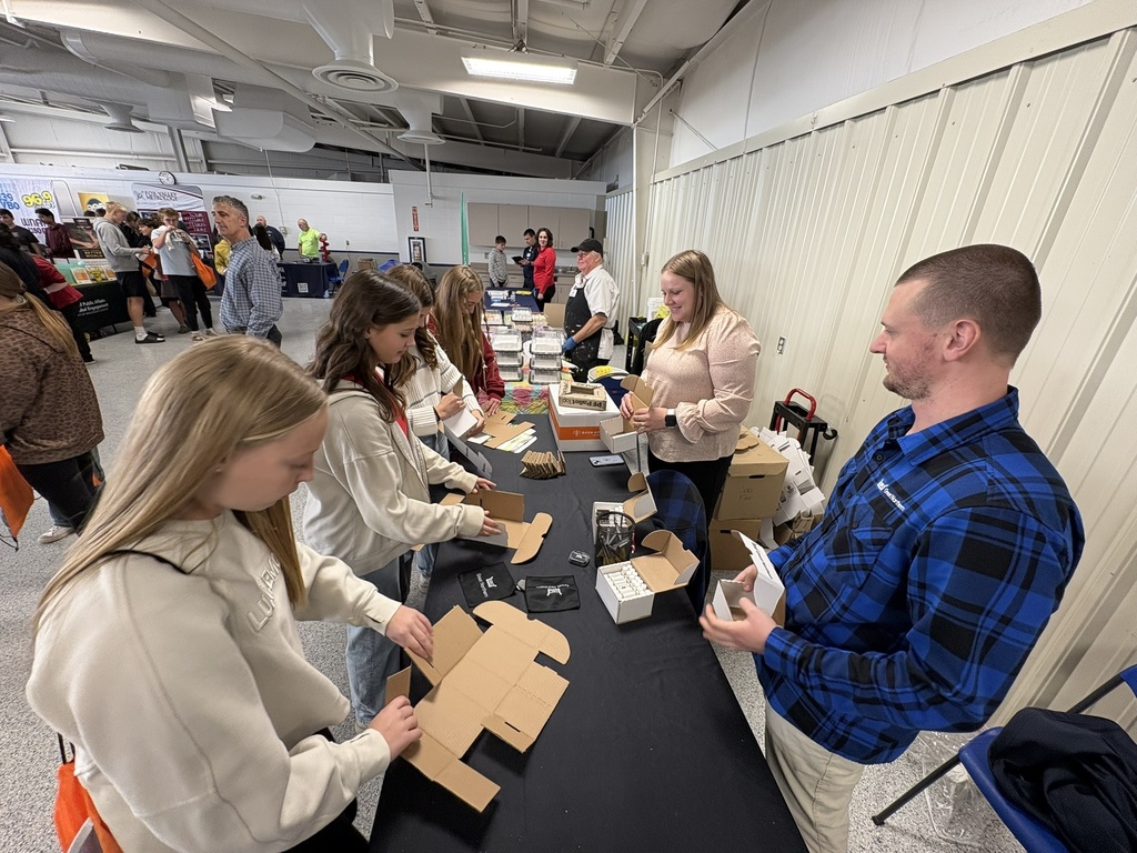 Middle school students folding boxes during a career expo with adults looking on.
