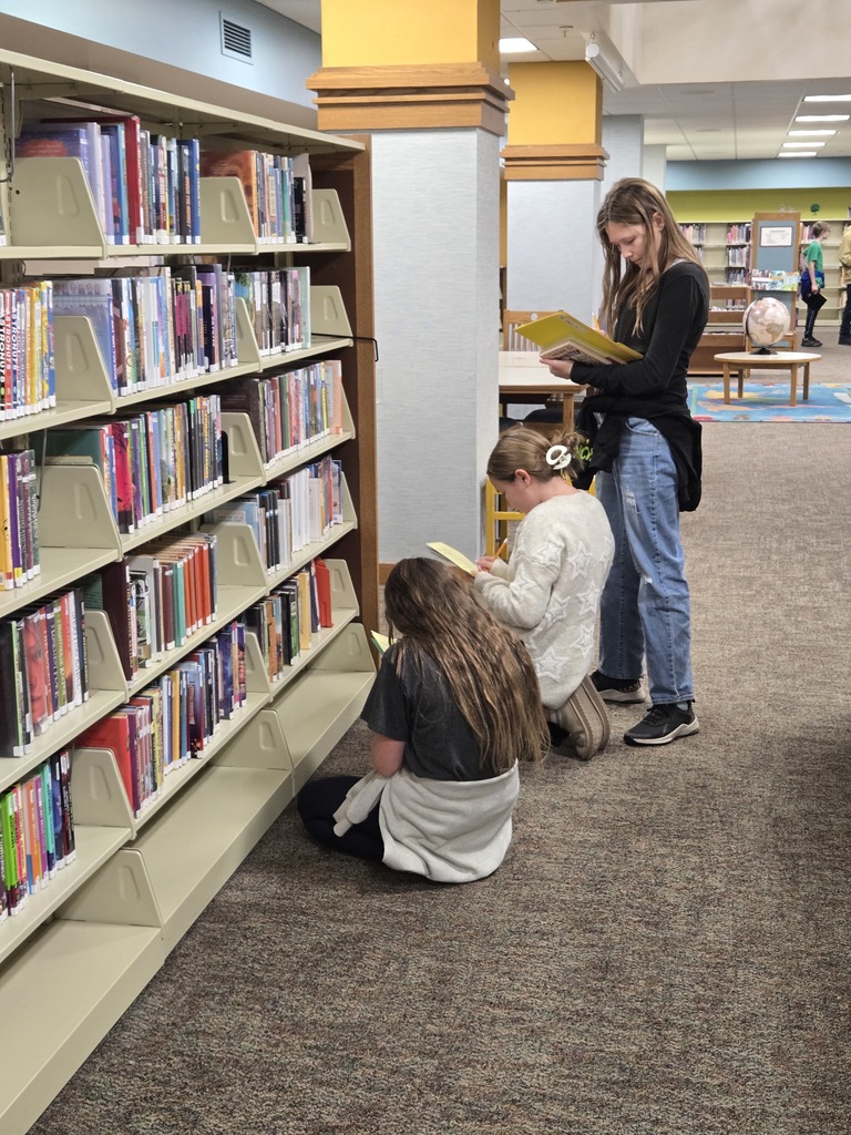 Students sitting in a media center on the floor while completing a scavenger hunt. 