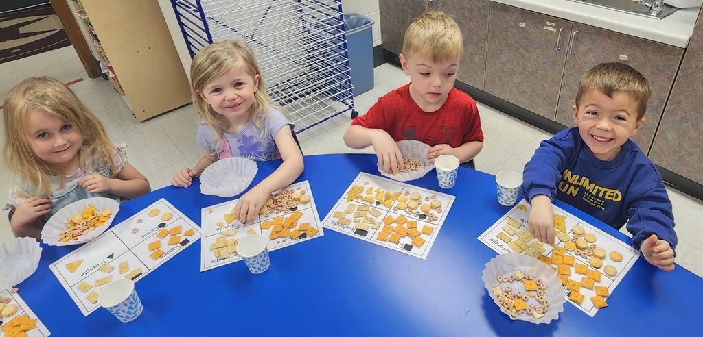 4 young elementary students, sitting at a table, sorting snacks by their shape.