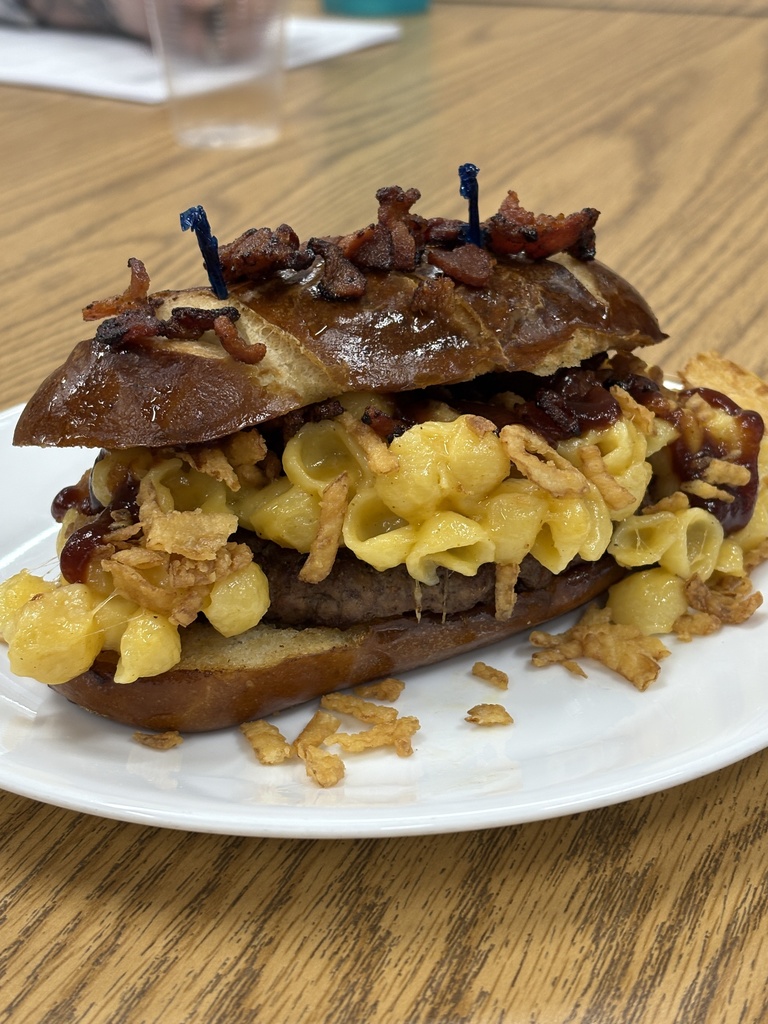 Picture of a burger on a bun with mac and cheese on it.