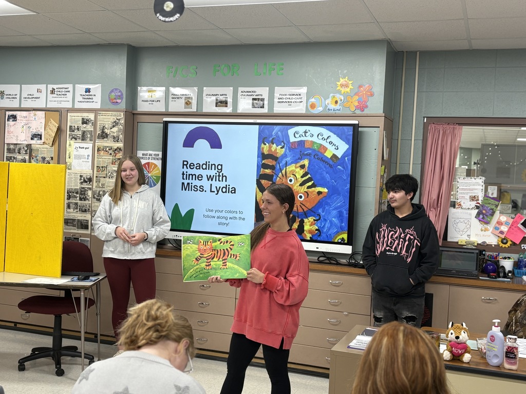Three high school students presenting and reading a children's book aloud.