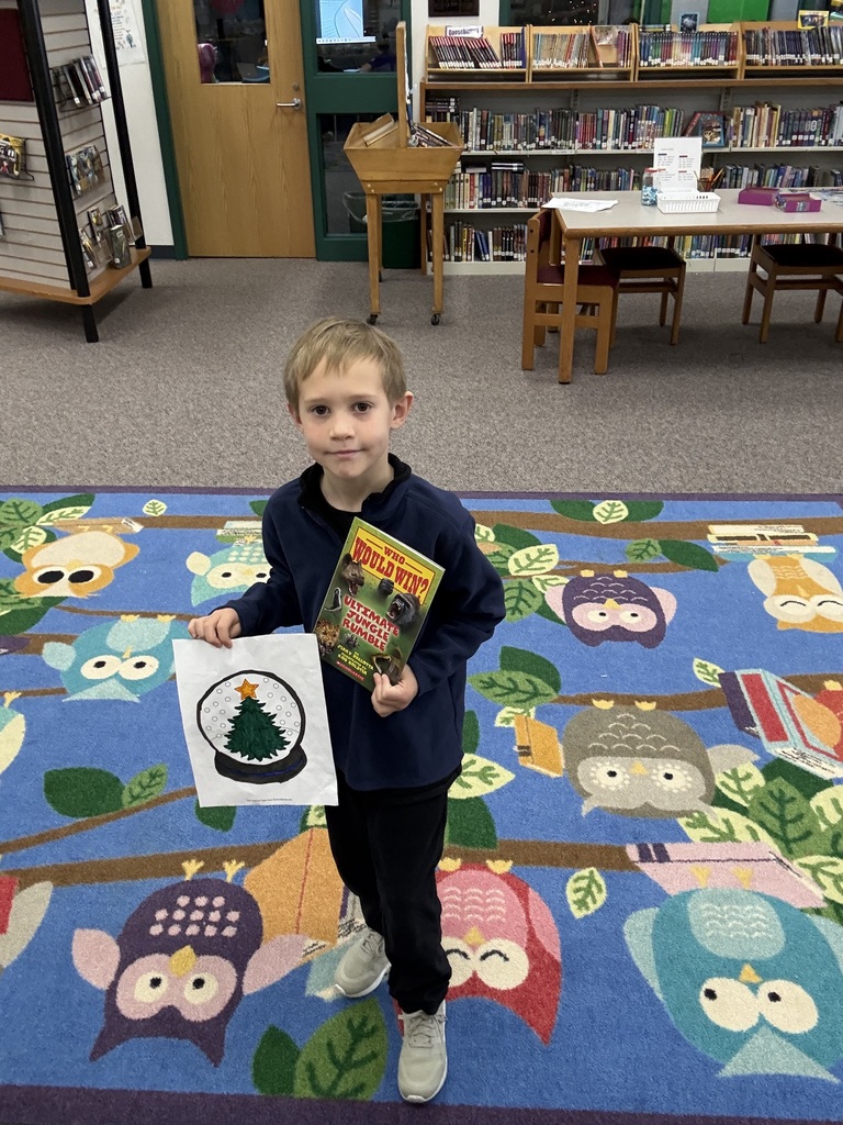 Elementary aged student holding a colored picture and a book.