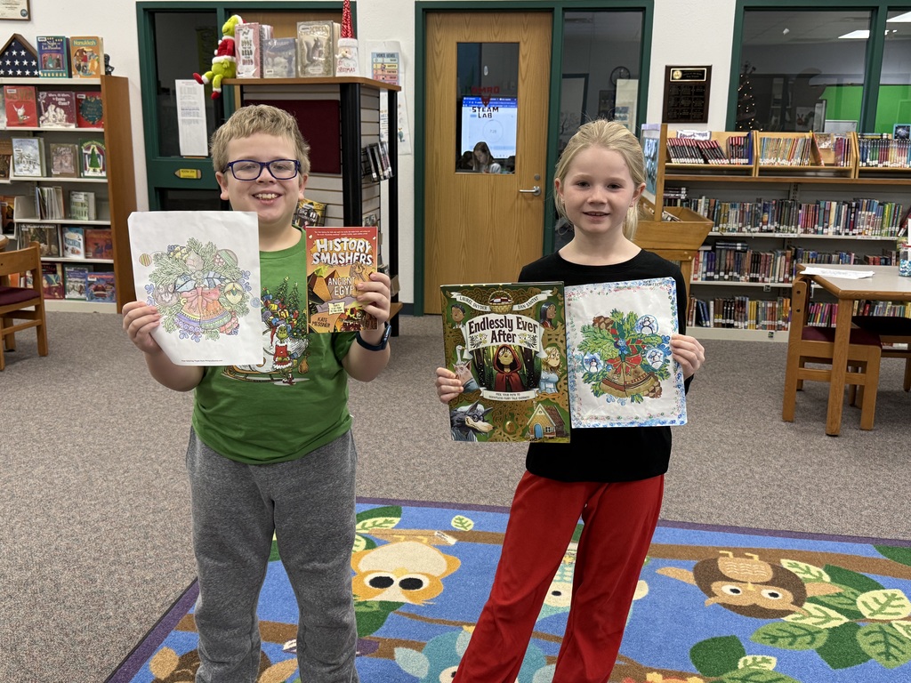 Two elementary aged students holding colored pictures and books.