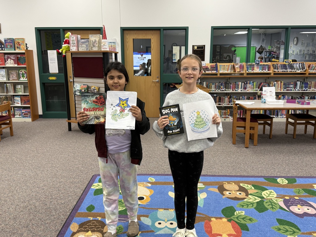 Two elementary aged students holding colored pictures and books.