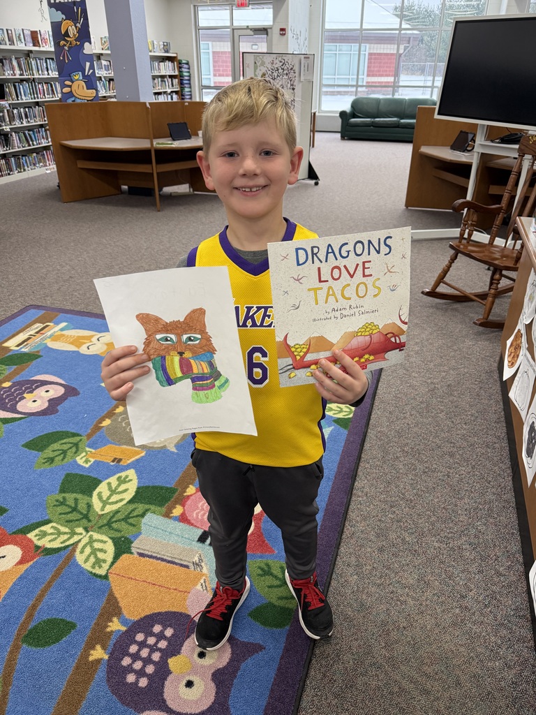 Elementary aged student holding a colored picture and a book.