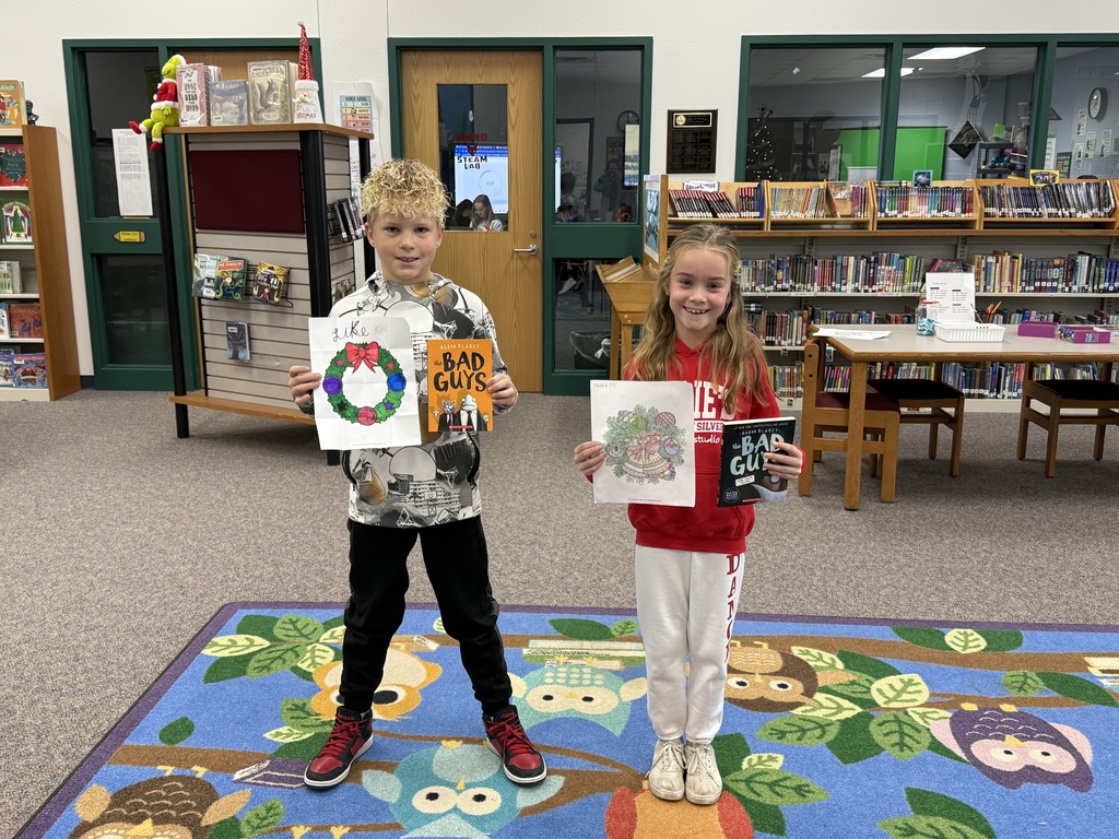 Two elementary aged students holding colored pictures and books.