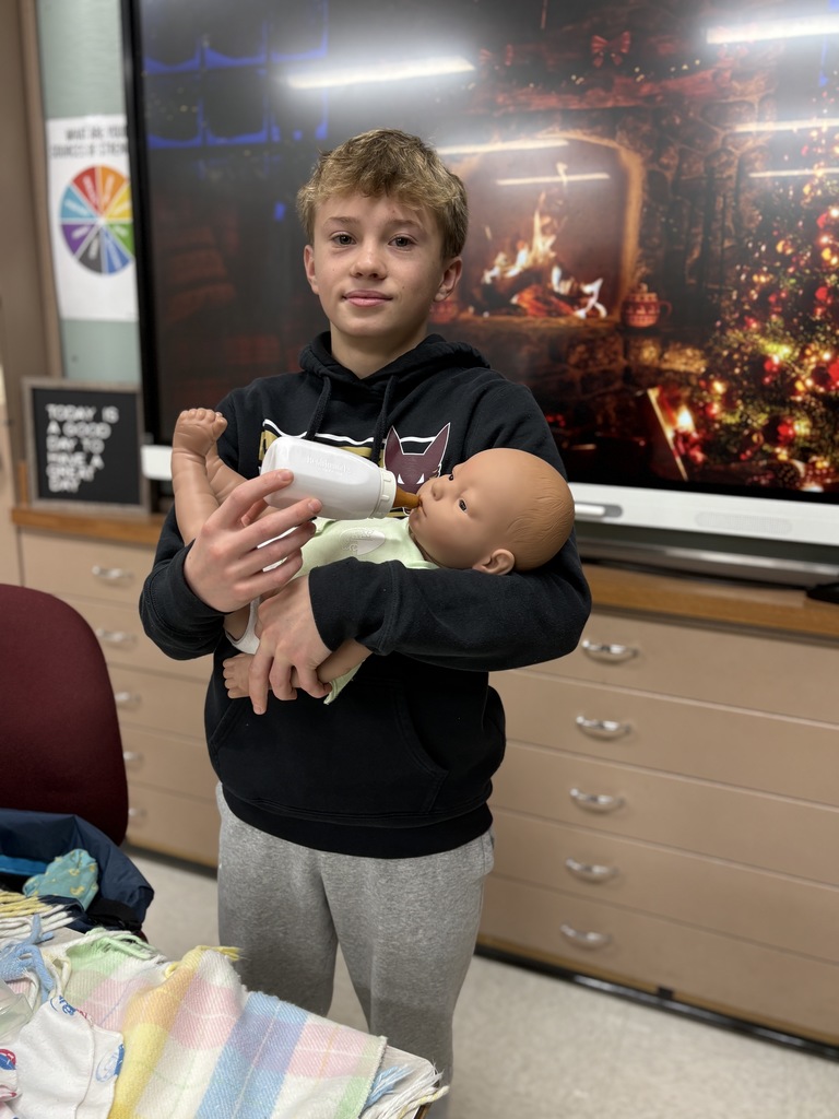 Middle school student holding and "feeding" a baby simulator.
