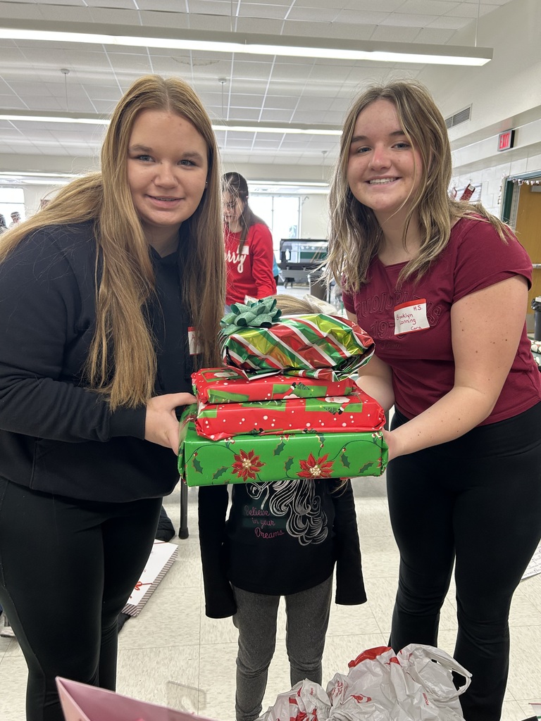 Two high school students with an elementary student between them, presents in front of the face.