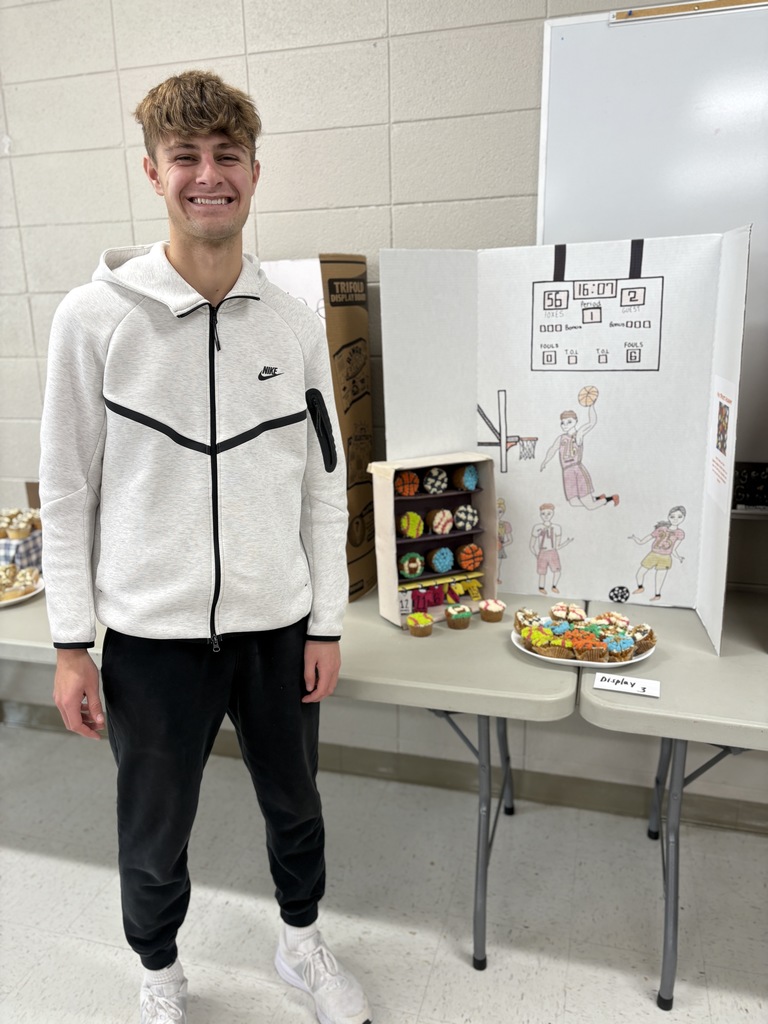 High school student standing by a cupcake display. Cupcakes are decorated with a sports theme. 