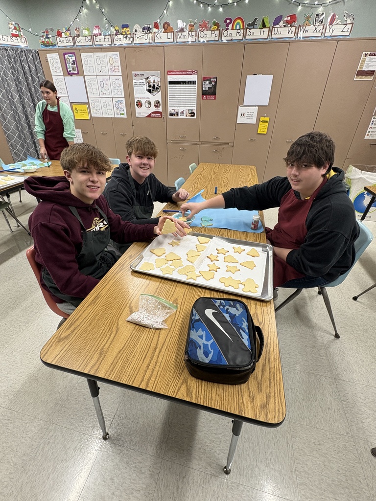 High school students sitting at a table with a baking pan of cookies in front of them. 
