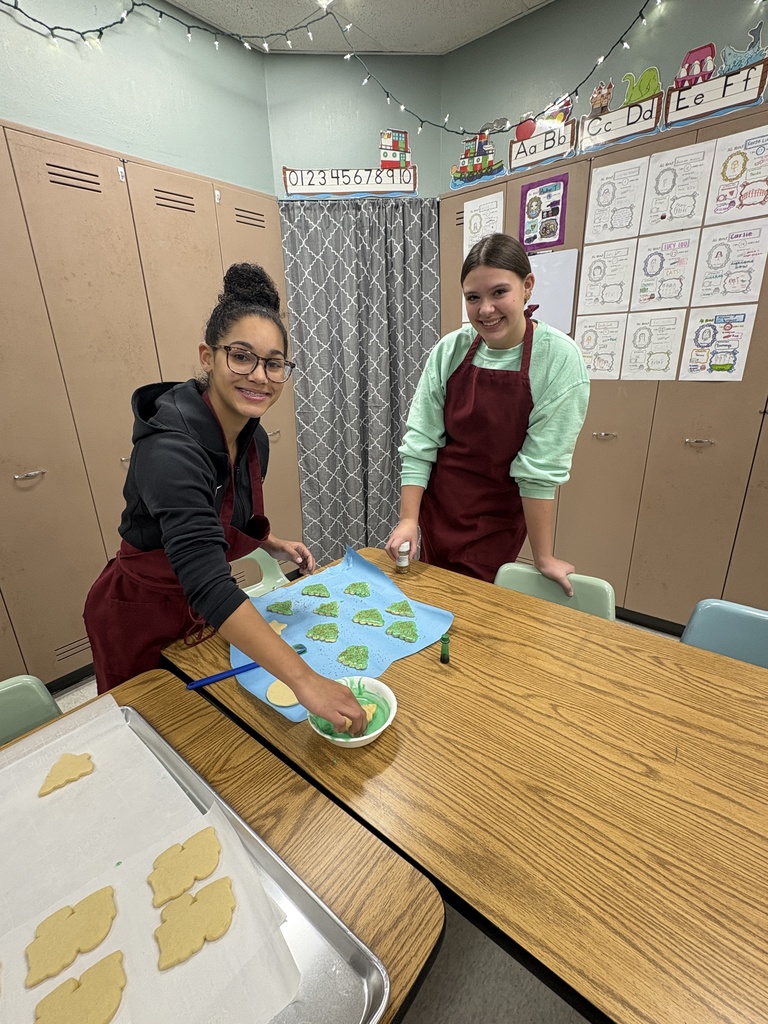 Two high school students frosting sugar cookies in green frosting.