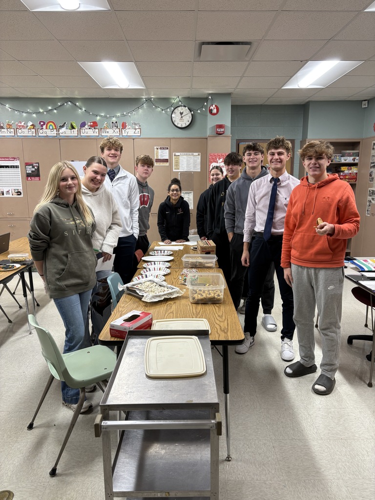 High school students surrounding a table that has baked goos on it.