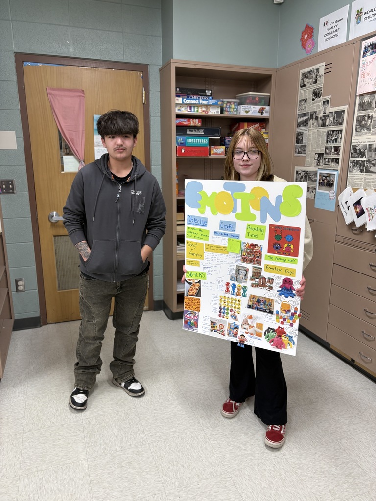 Two high school students hold a poster detailing their lesson plan about emotions.