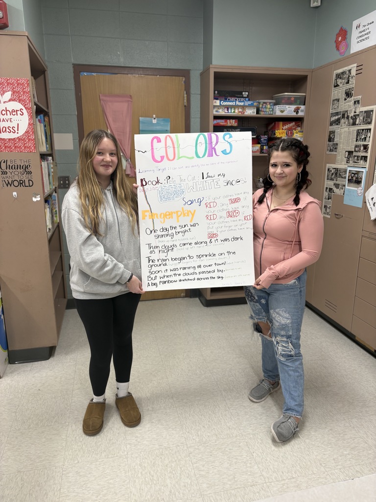 Two high school students hold a poster detailing their lesson plan about colors.