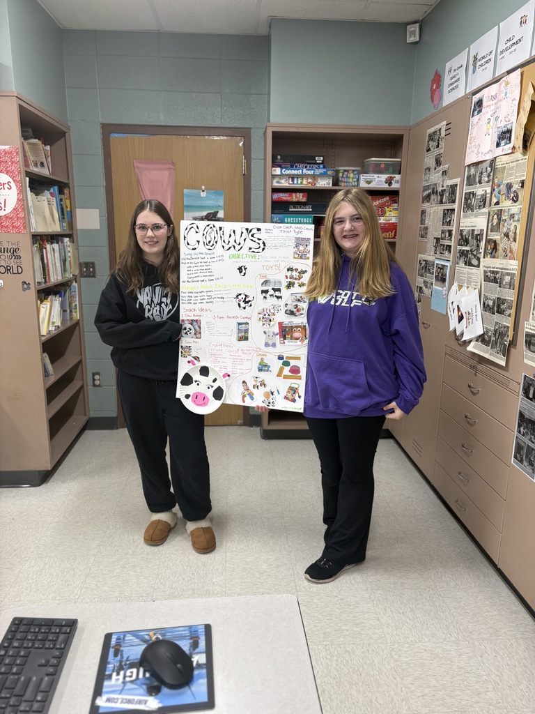 Two high school students hold a poster detailing their lesson plan about cows.